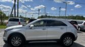 White SUV parked in a lot with power lines and blue sky above; other cars visible in background.