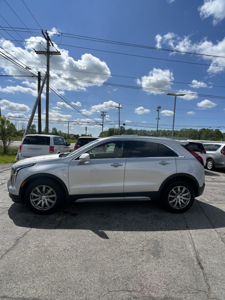 White SUV parked in a lot with power lines and blue sky above; other cars visible in background.