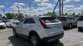White SUV in a busy car dealership lot, with power lines overhead and a bright blue sky with clouds behind it.