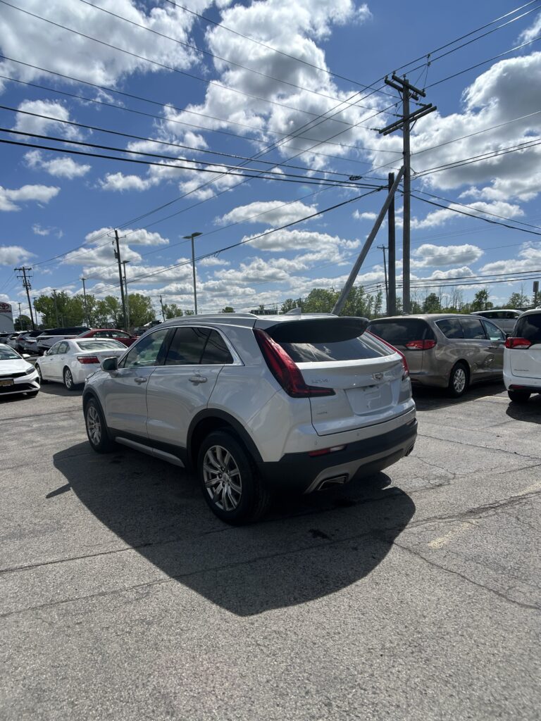 White SUV in a busy car dealership lot, with power lines overhead and a bright blue sky with clouds behind it.