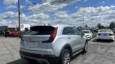 White Cadillac SUV in a dealership parking lot with other cars and a blue sky with clouds above.