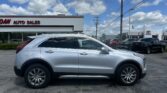 Silver SUV parked in a car dealership lot, with the 'AUTO SALES' building in the background under a blue sky with clouds.