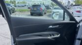 Interior car door in the foreground with an exterior parking lot full of cars and a blue, cloudy sky beyond. The open door frames the scene outside.