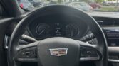 View from the driver’s seat of a Cadillac, showing the steering wheel and dashboard with a sunny parking lot outside the windshield.