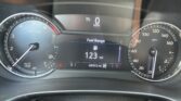 Car dashboard showing 0 mph, tachometer on left, and center digital display with fuel range and odometer info.