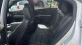 Interior of a silver SUV showing black leather rear seats with headrests and open rear door, parking lot visible outside.