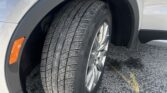 Close-up of a gray SUV's front wheel well showing a tire, alloy wheel, orange side marker, and Cadillac badge on the fender.