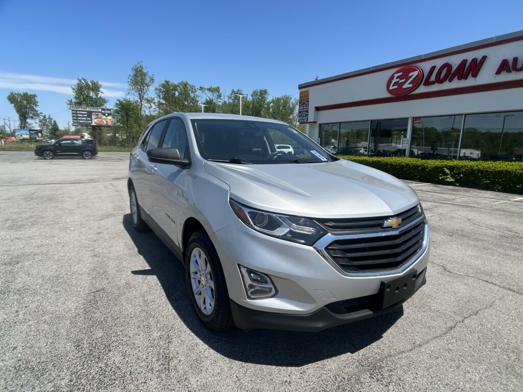 Silver Chevrolet SUV in the foreground at a car lot with an EZ Loan Auto storefront under a clear blue sky, daytime sun.