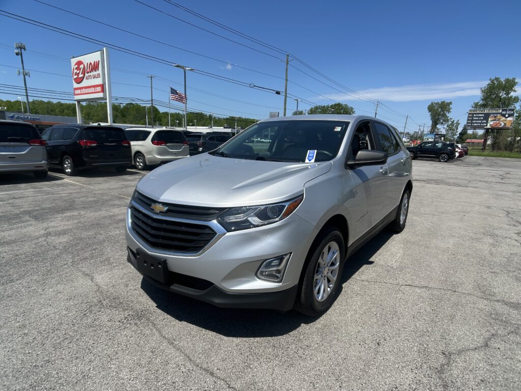 Silver SUV in the foreground at a dealership lot, with a large EZ LOAN Auto Sales sign and blue sky in the background.