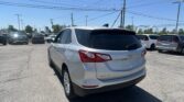 Silver Chevrolet Equinox SUV in a crowded parking lot under a clear blue sky with power lines overhead