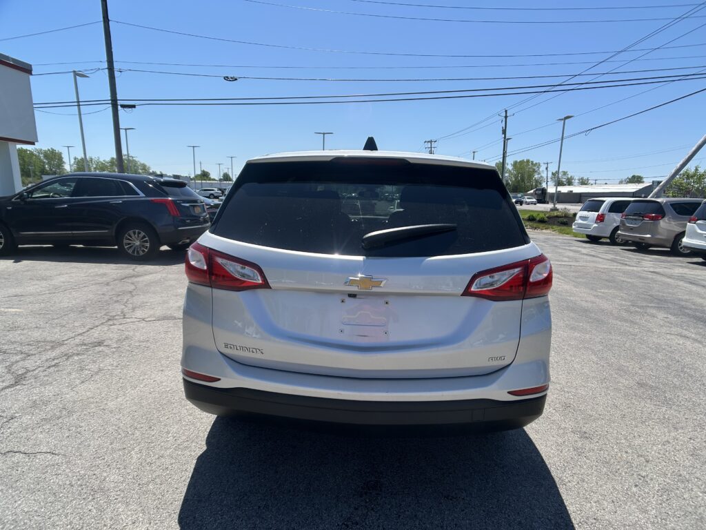 Back of a white Chevrolet Equinox parked in a lot, with other cars and power lines overhead against a blue sky.