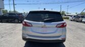 Back of a white Chevrolet Equinox parked in a lot, with other cars and power lines overhead against a blue sky.