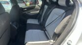 Rear passenger seat in a car with light gray quilted upholstery and visible seat belts in a parking lot inside the vehicle's cabin.
