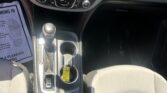 Center console of a car interior featuring a touchscreen infotainment system, climate controls, hazard button, gear shifter, and two cup holders in front of the gear lever.