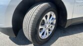 Close-up of a car wheel and tire in the wheel well, on a light-colored vehicle parked on pavement.