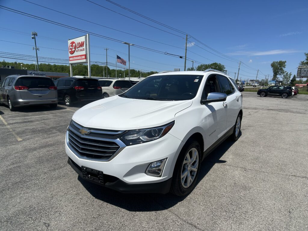 White Chevrolet SUV in the foreground at a car dealership lot with a tall EZ Loan Auto Sales sign and other vehicles nearby.