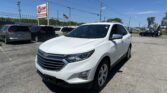 White Chevrolet SUV in the foreground at a car dealership lot with a tall EZ Loan Auto Sales sign and other vehicles nearby.