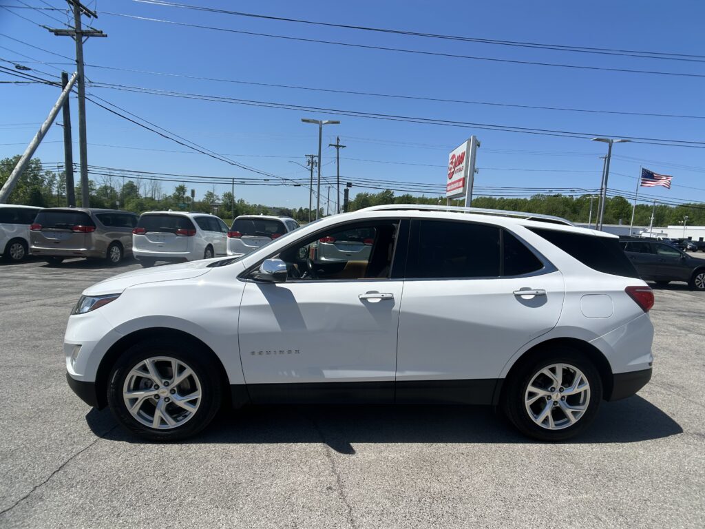 White Chevrolet Equinox in a dealership lot among other minivans, with power lines and a clear blue sky overhead.