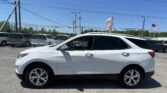 White Chevrolet Equinox in a dealership lot among other minivans, with power lines and a clear blue sky overhead.