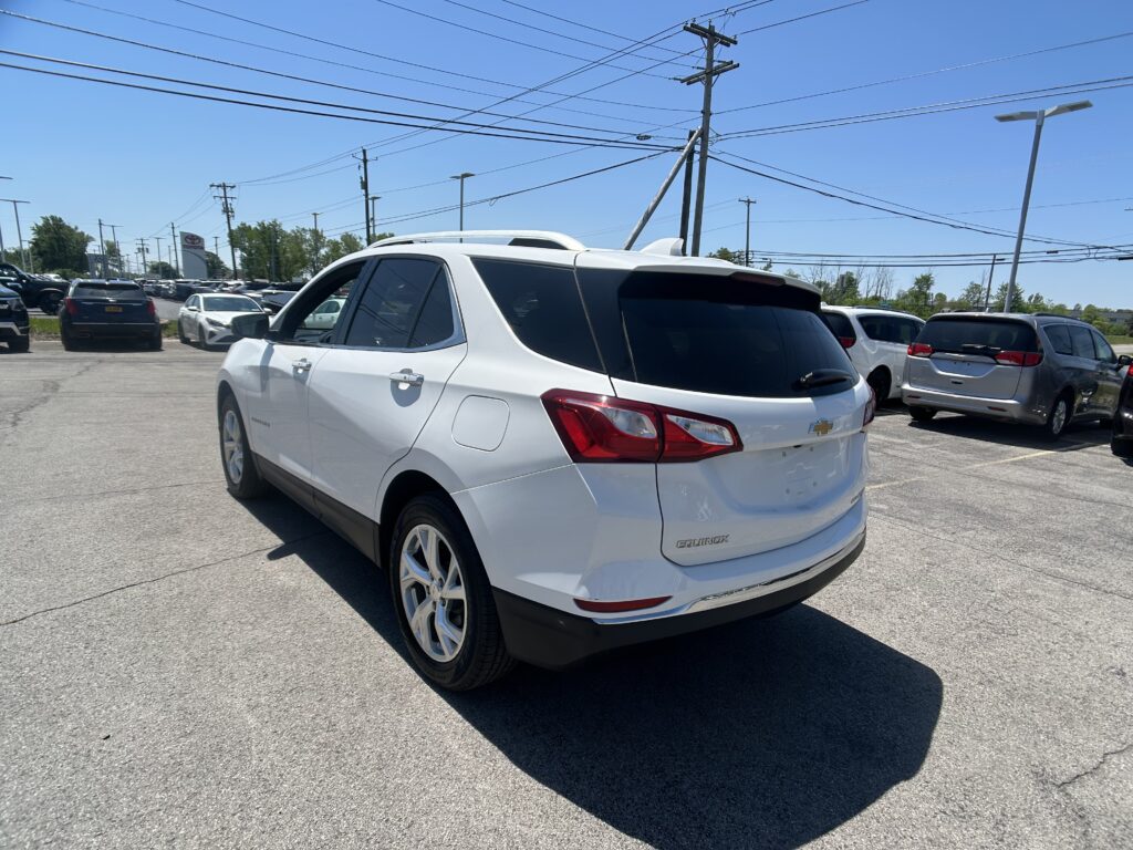 White Chevrolet Equinox SUV parked in a dealership lot with other cars and overhead power lines under a clear blue sky.