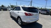 White Chevrolet Equinox SUV parked in a dealership lot with other cars and overhead power lines under a clear blue sky.