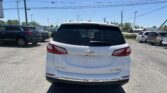 Rear view of a white Chevrolet SUV in a busy parking lot on a sunny day, with other cars and overhead power lines in the background.