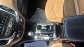 Tan leather car interior with the front passenger seat, center console, and a newspaper resting on the floor mat by the seat.