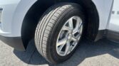 Close-up of a car tire mounted on a silver alloy wheel inside the wheel well of a light-gray SUV on an asphalt surface.