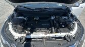 Front of a white car with the hood open, revealing the engine bay and battery components in daylight