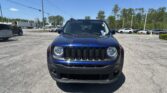 Front view of a blue Jeep Wrangler in a sunny parking lot with other cars and trees in the background.