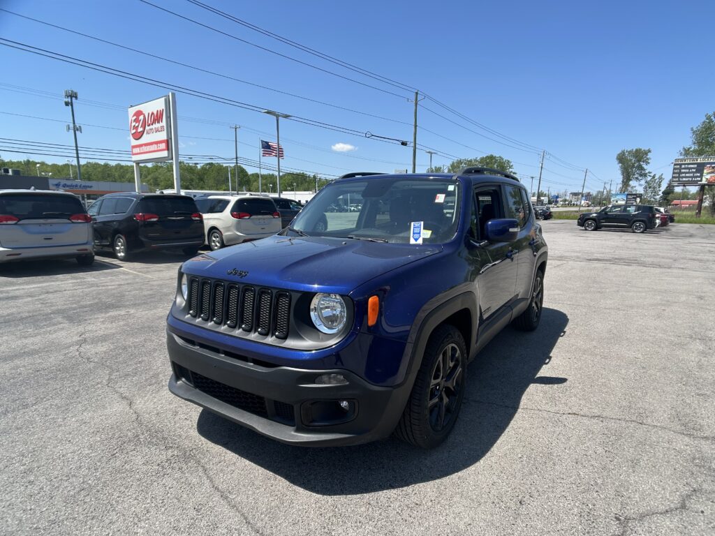 Blue Jeep SUV in a crowded car dealership lot with other cars, signage, and power lines under a clear blue sky.