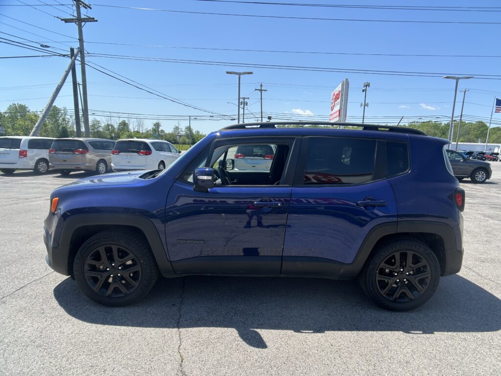 Blue GMC Yukon Denali parked in a dealership lot with white vans and power lines overhead.