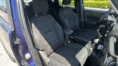 Blue SUV interior with two front seats and headrests; steering wheel on the right, parked in a lot with green bushes outside the window.