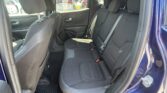 Rear seating area of a dark fabric SUV with three-seat bench, adjustable headrests, and visible seatbelts; door panel and window to the left, outside cars visible.