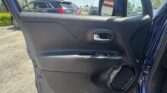 Interior view of a car door panel with window controls and silver door handle; outside is a parking lot with several vehicles and a blue sky.