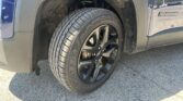 Close-up of a blue pickup truck's front wheel, showing the tire, alloy rim, brake rotor, and dirty wheel well with a visible suspension coil spring behind it.