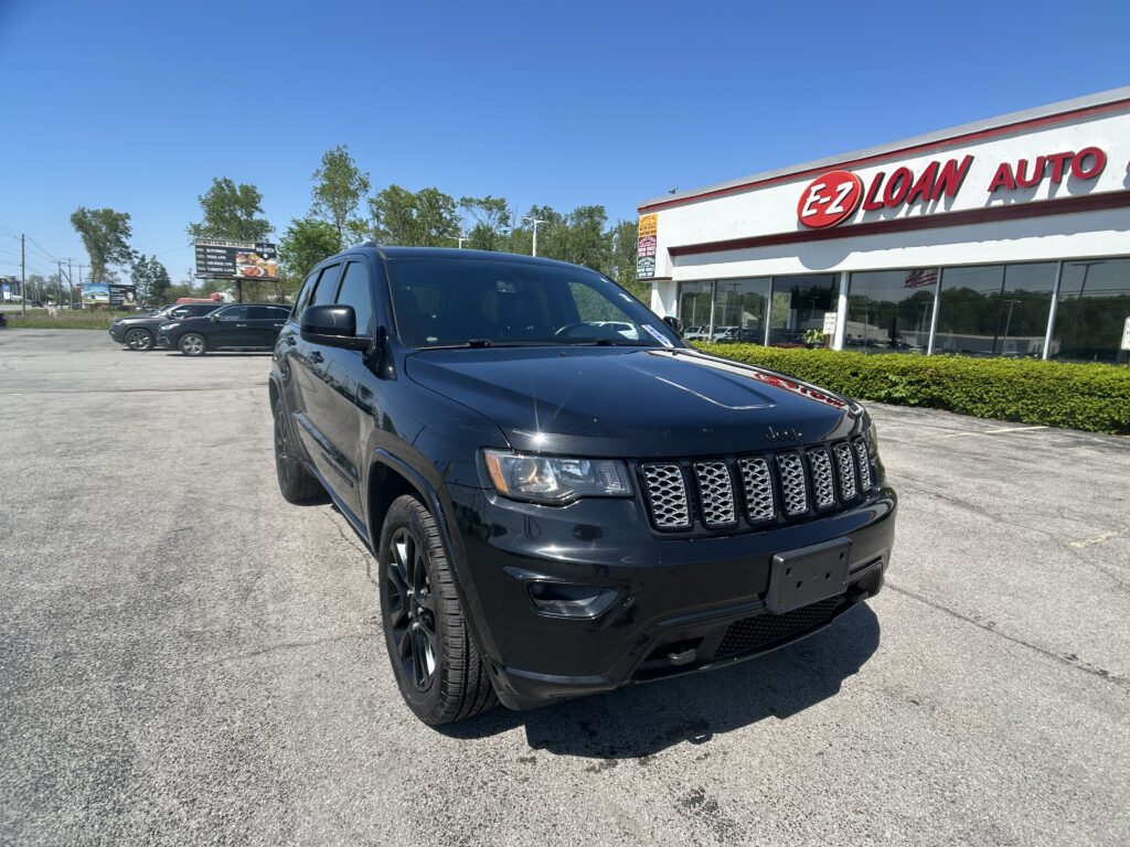 Black Jeep SUV parked diagonally in a dealership lot with an EZ LOAN AUTO sign on the building and a clear blue sky ahead.