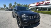 Black Jeep SUV parked diagonally in a dealership lot with an EZ LOAN AUTO sign on the building and a clear blue sky ahead.