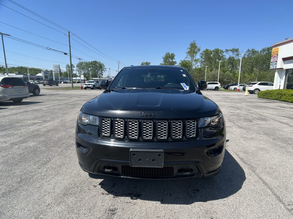 Front view of a black Jeep SUV in a sunny car dealership lot, centered in the frame with other vehicles in the background