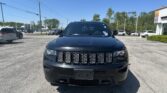 Front view of a black Jeep SUV in a sunny car dealership lot, centered in the frame with other vehicles in the background