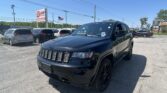 Black Jeep SUV in the foreground of a car dealership lot with other vehicles, an EZ Loan sign, and an American flag against a clear blue sky.