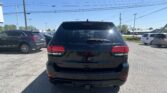 Rear view of a black Jeep SUV parked in a lot with other cars and a clear blue sky above, power lines overhead.