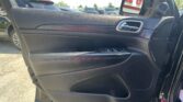 Interior of a car door with a chrome door handle, wood-like trim, control buttons, and a side mirror showing a parking lot outside.