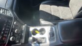 Interior of a car: center console with gear shifter, cup holders, climate controls, and beige seats.
