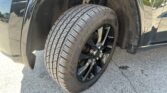 Front wheel and tire of a black SUV, showing the alloy wheel and wheel well with dirt.