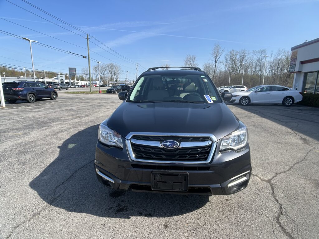 Front view of a dark gray Subaru SUV in a dealership parking lot on a sunny day.