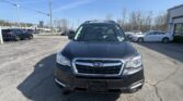 Front view of a dark gray Subaru SUV in a dealership parking lot on a sunny day.