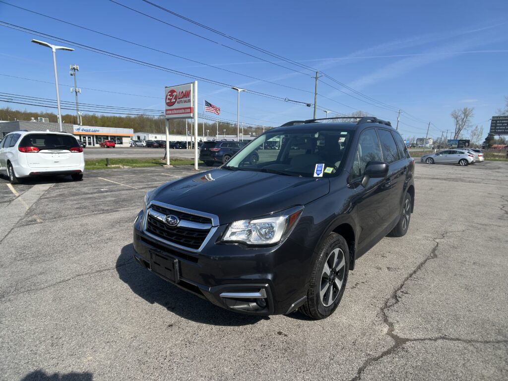 Dark blue SUV in a dealership lot with an EZ Loan Auto Sales sign and a waving American flag in the background