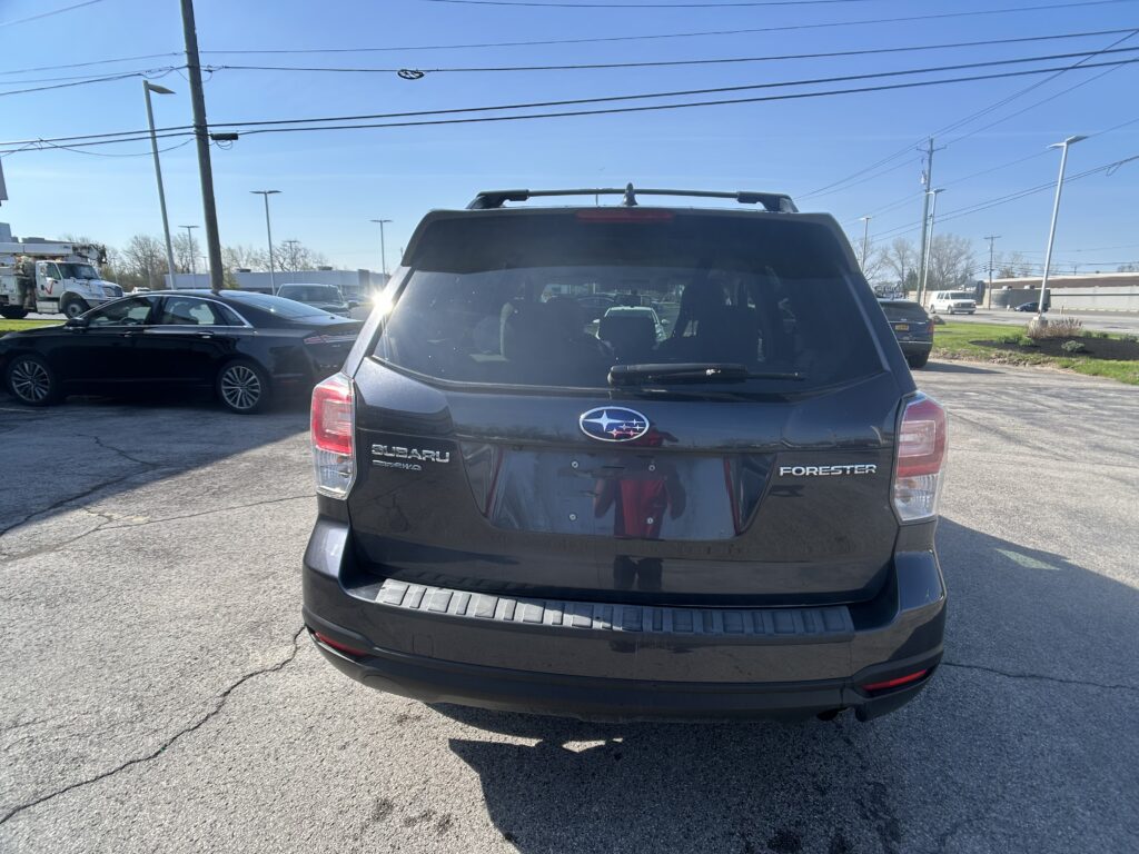 Rear view of a black Subaru Forester in a parking lot, with other cars and power lines against a clear blue sky.