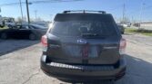 Rear view of a black Subaru Forester in a parking lot, with other cars and power lines against a clear blue sky.